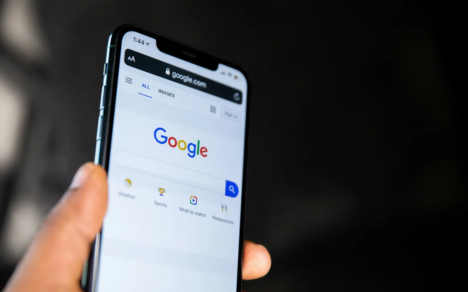 Dłoń trzyma smartfon ze stroną główną wyszukiwarki Google