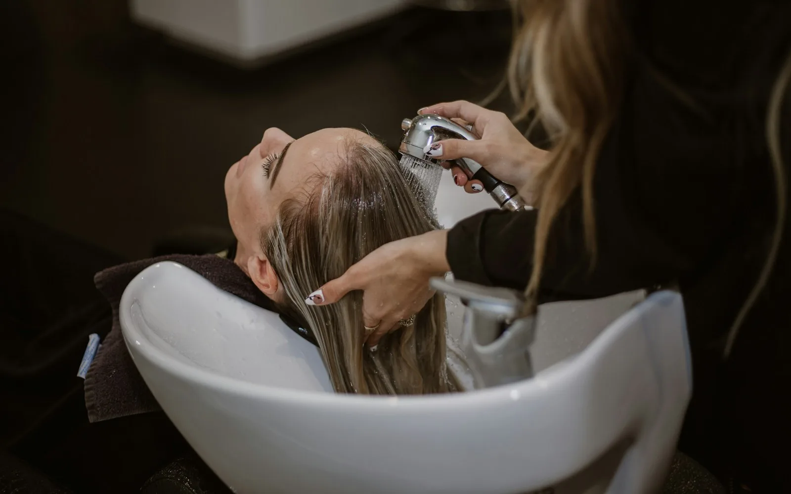 Fryzjerka myje klientce włosy przy umywalce w salonie